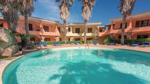 A pool surrounded by lounge chairs and palm trees, with a building in the background. - Tranquile Palau Green Village Studio Prem 2 person plus possible extra Child-Bed (Palau)