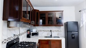 Una cocina con armarios de madera oscura, un refrigerador negro, una estufa a gas y un microondas.
