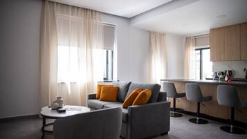 A modern living room with a grey sofa, two yellow cushions, a small round table, and a bar area with two grey chairs.