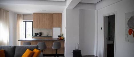 A modern hotel room with a grey sofa, a small kitchen area, and a suitcase on the floor.