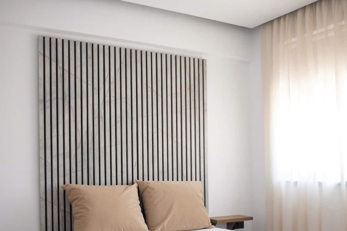 Een moderne slaapkamer met een bed, beige kussens, een nachtkastje en een hoofdbord met verticale strepen.
