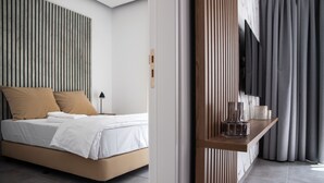 A modern bedroom with a bed, a bedside table with a lamp, and a view of the outside through a window with curtains. - LE BOUQUET LUXURY SUITES  (Nicosia)