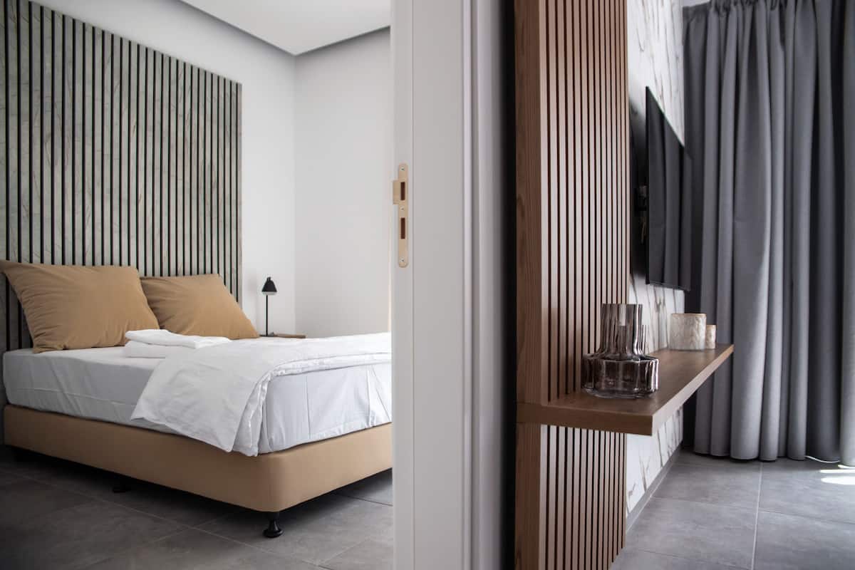 Een moderne slaapkamer met een bed, een nachtkastje met een lamp en uitzicht buiten door een raam met gordijnen.