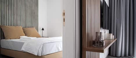 A modern bedroom with a bed, a bedside table with a lamp, and a view of the outside through a window with curtains.