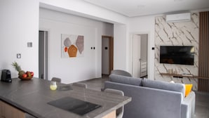 A modern living room with a grey sofa, a dining area with a marble table, and a TV mounted on a marble wall. - LE BOUQUET LUXURY SUITES  (Nicosia)
