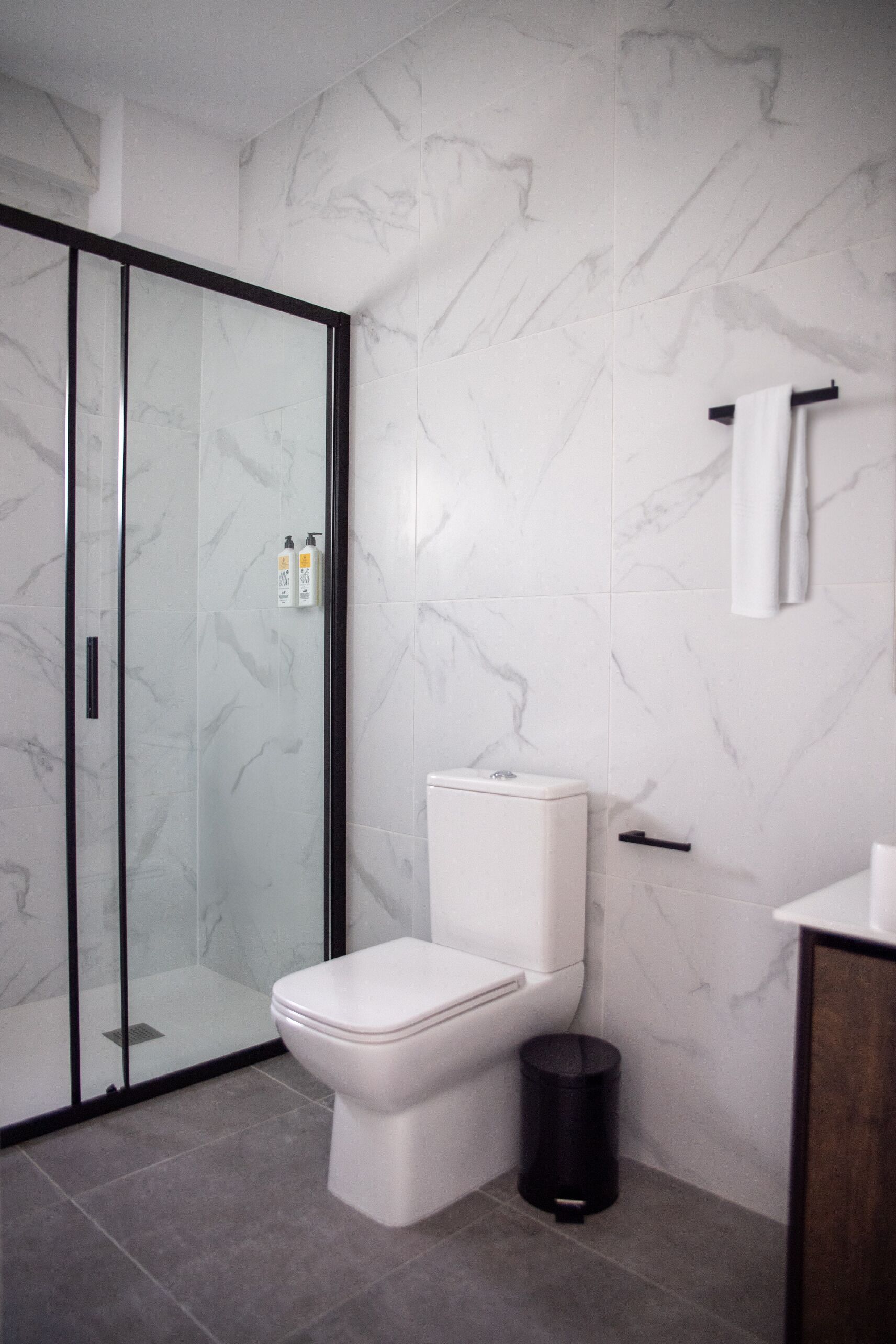 A modern bathroom with a toilet, a glass shower enclosure, and a marble-patterned wall.