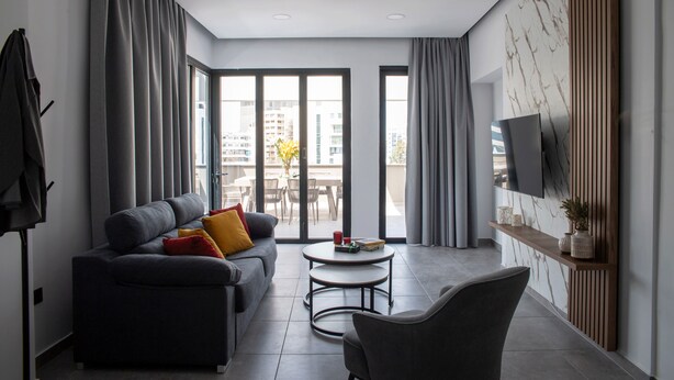 A modern living room with a sofa, a coffee table, and a TV mounted on the wall. - LE BOUQUET LUXURY SUITES  (Nicosia)