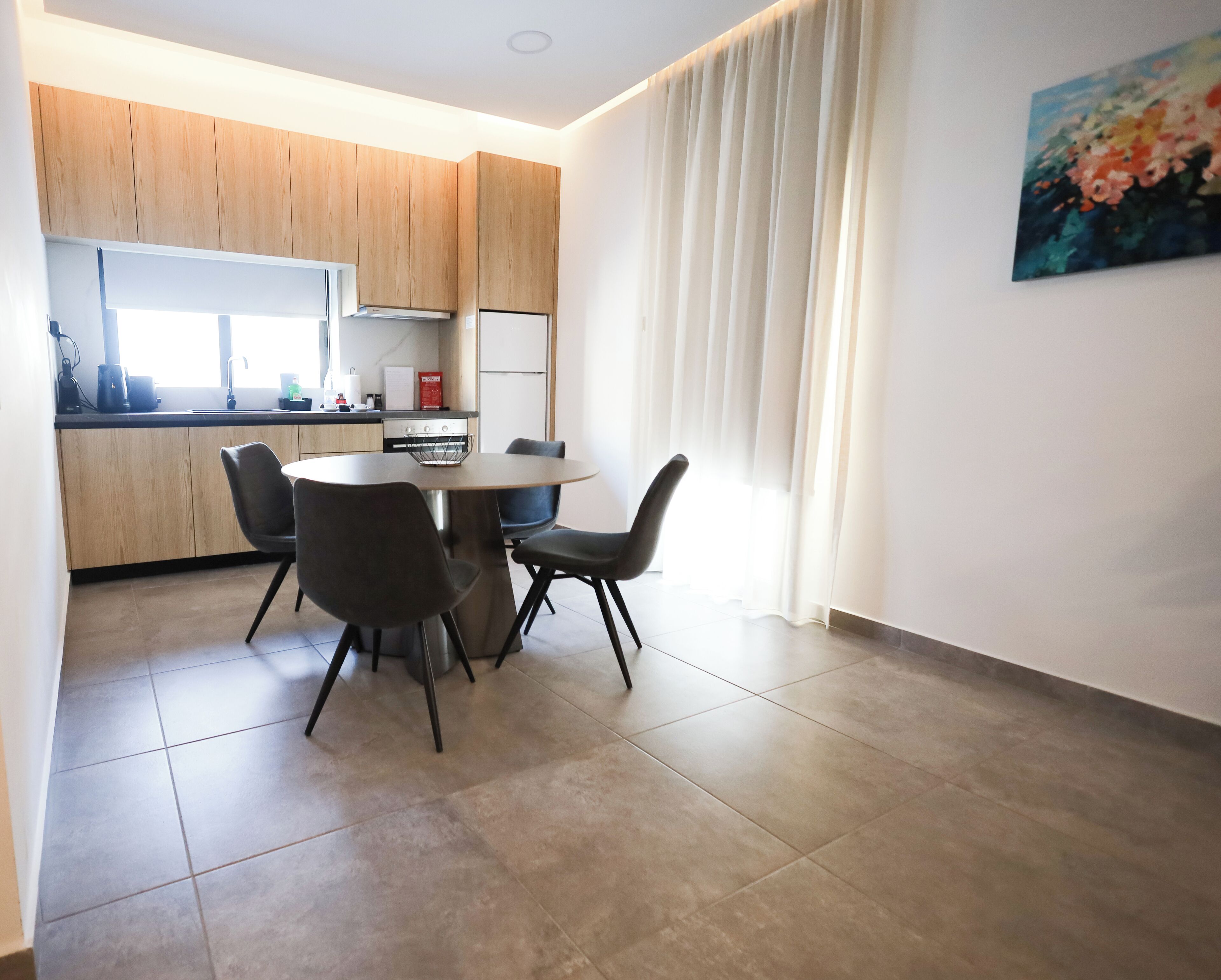 Una cocina moderna con armarios de madera, una mesa de comedor con cuatro sillas y un ventanal con cortinas.