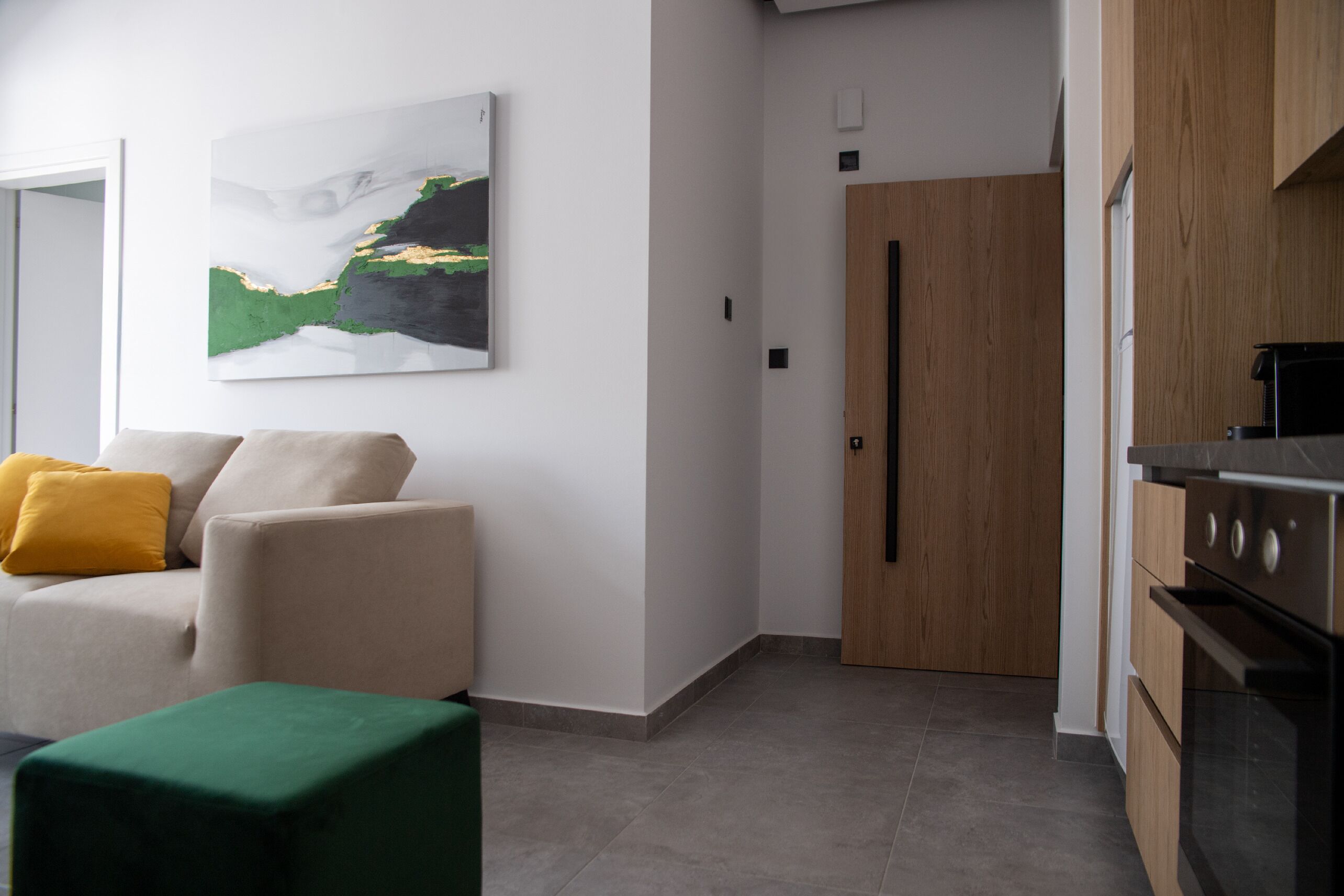 Un soggiorno moderno con un divano, un pouf verde e un quadro appeso al muro.
