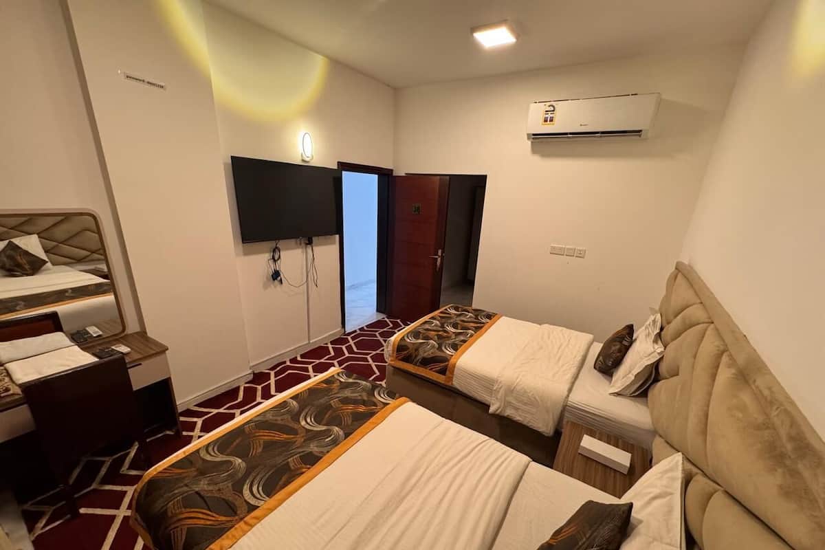 Quarto de hotel com duas camas, uma escrivaninha, uma cadeira, uma televisão e um ar condicionado.