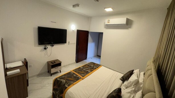 Une chambre d’hôtel comprenant un lit, un téléviseur fixé au mur, un appareil de climatisation, un bureau avec une lampe et une armoire.