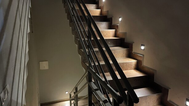 A staircase with a black railing, wooden steps, and wall-mounted lights. - Akhard Haus (Buea)