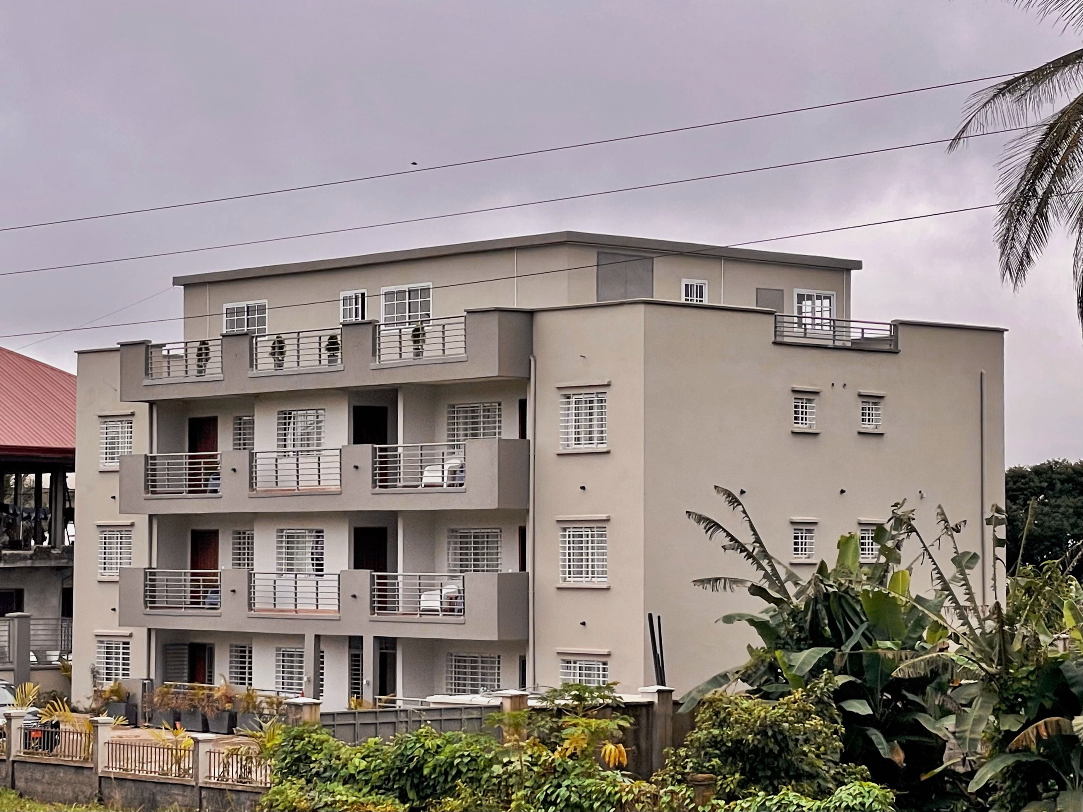 Un edificio de varios pisos con balcones, techo plano y entrada protegida por una reja.