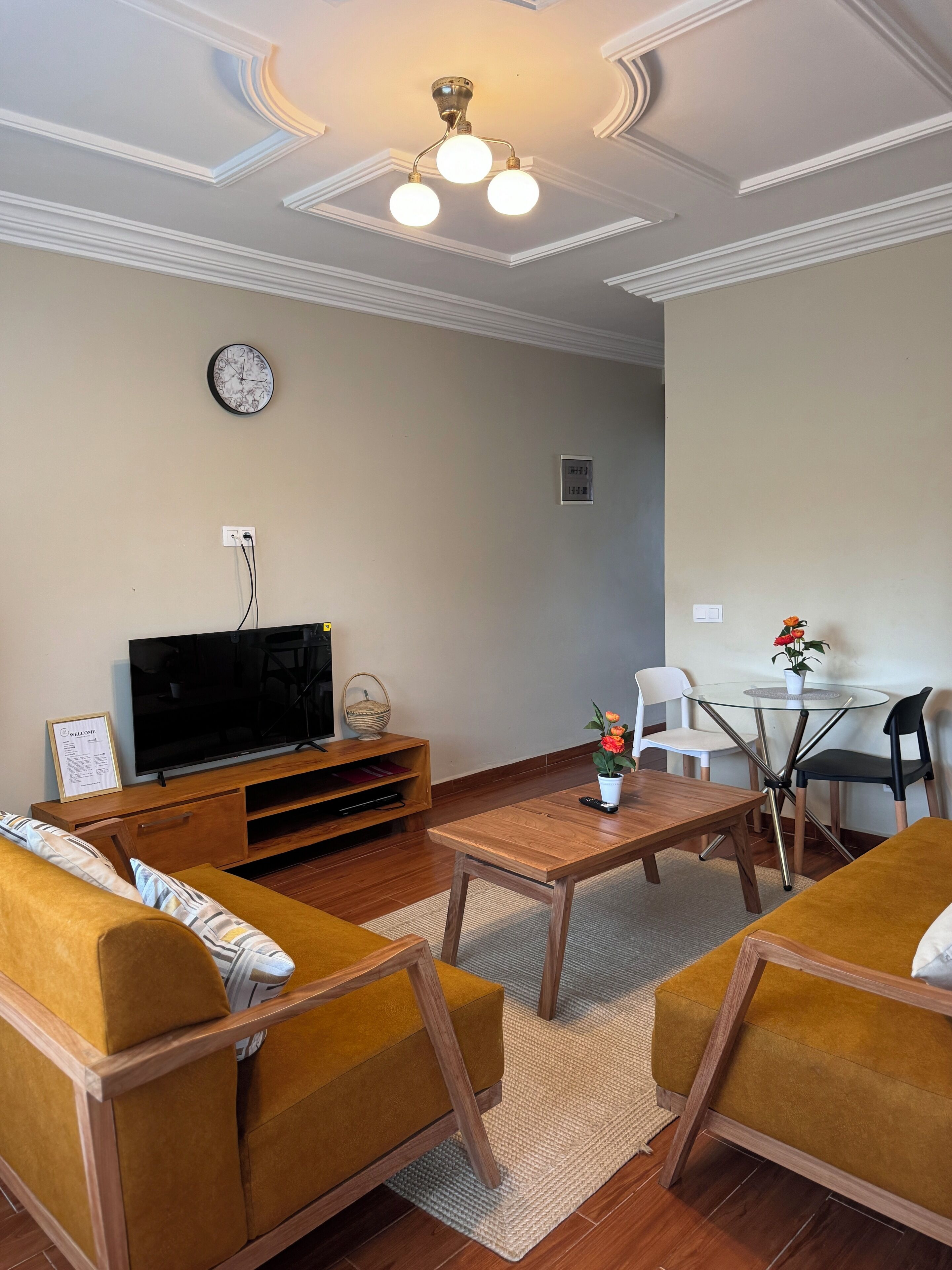 A living room with a TV, sofa, coffee table, and a dining area with chairs and a small table.