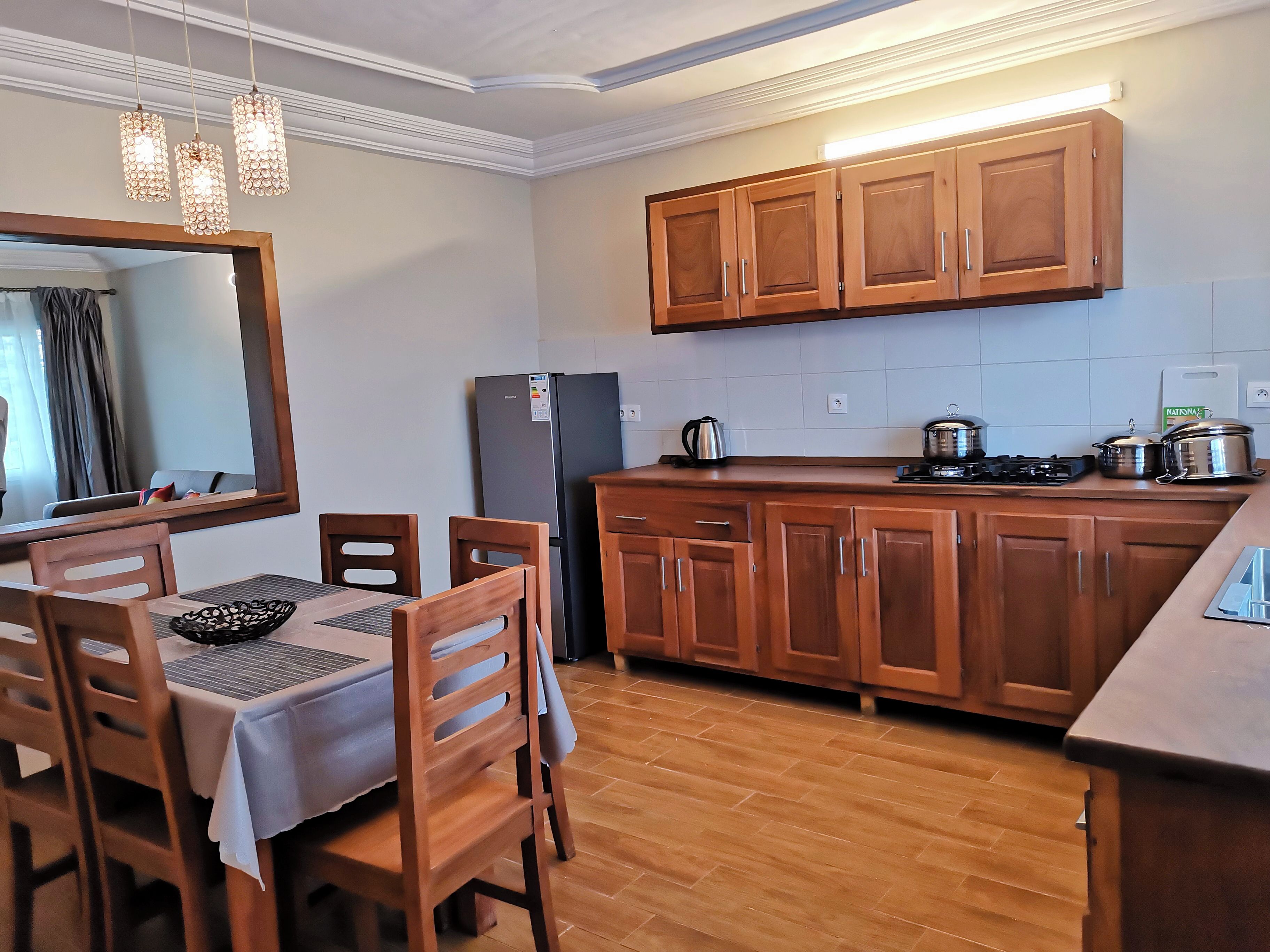 A compact kitchen with wooden cabinets, a refrigerator, a stove, and a dining area with a table and chairs.