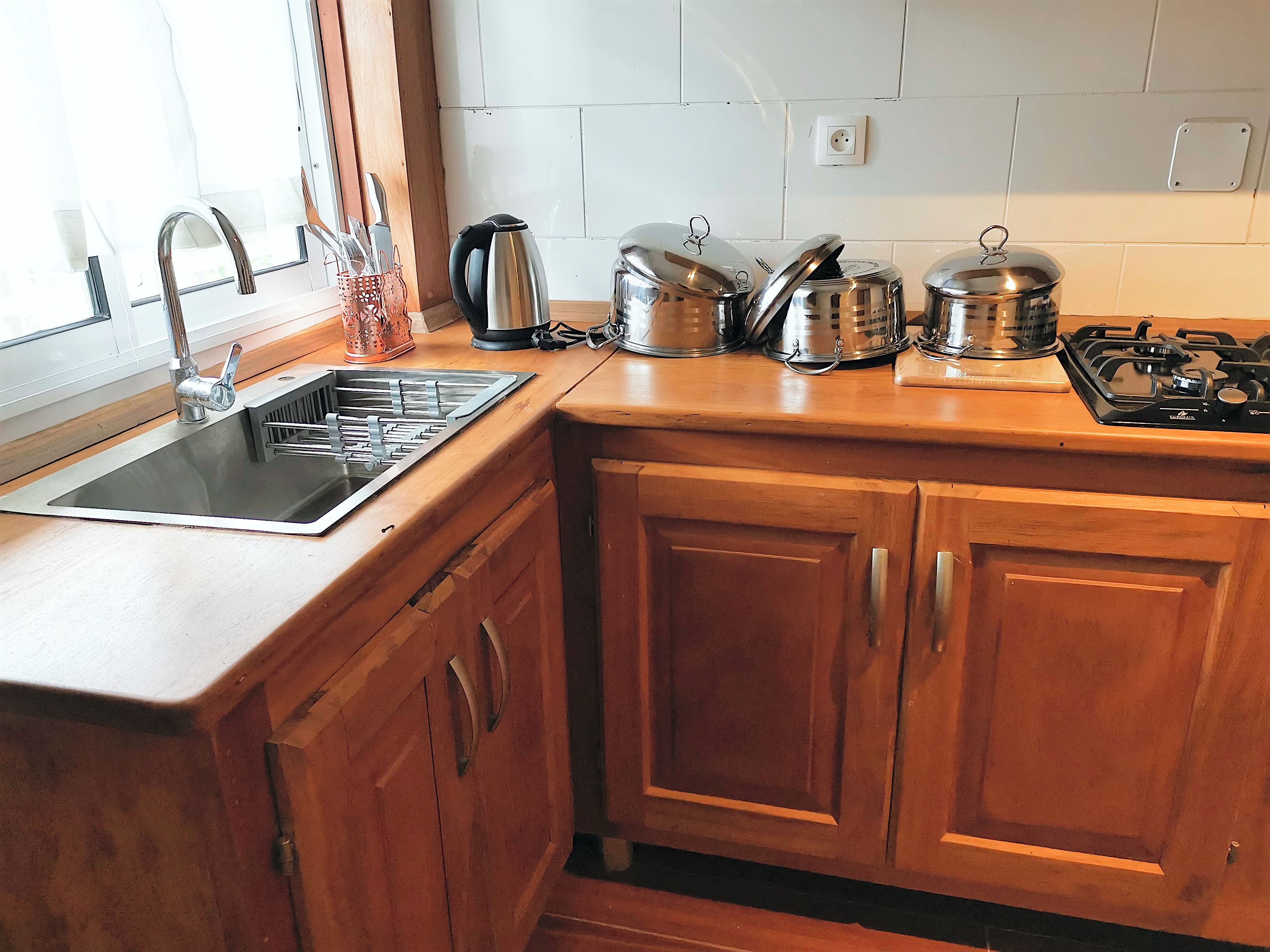 Une cuisine équipée d’un évier en acier inoxydable, de meubles de rangement en bois, d’une cuisinière à gaz et de divers appareils électroménagers.