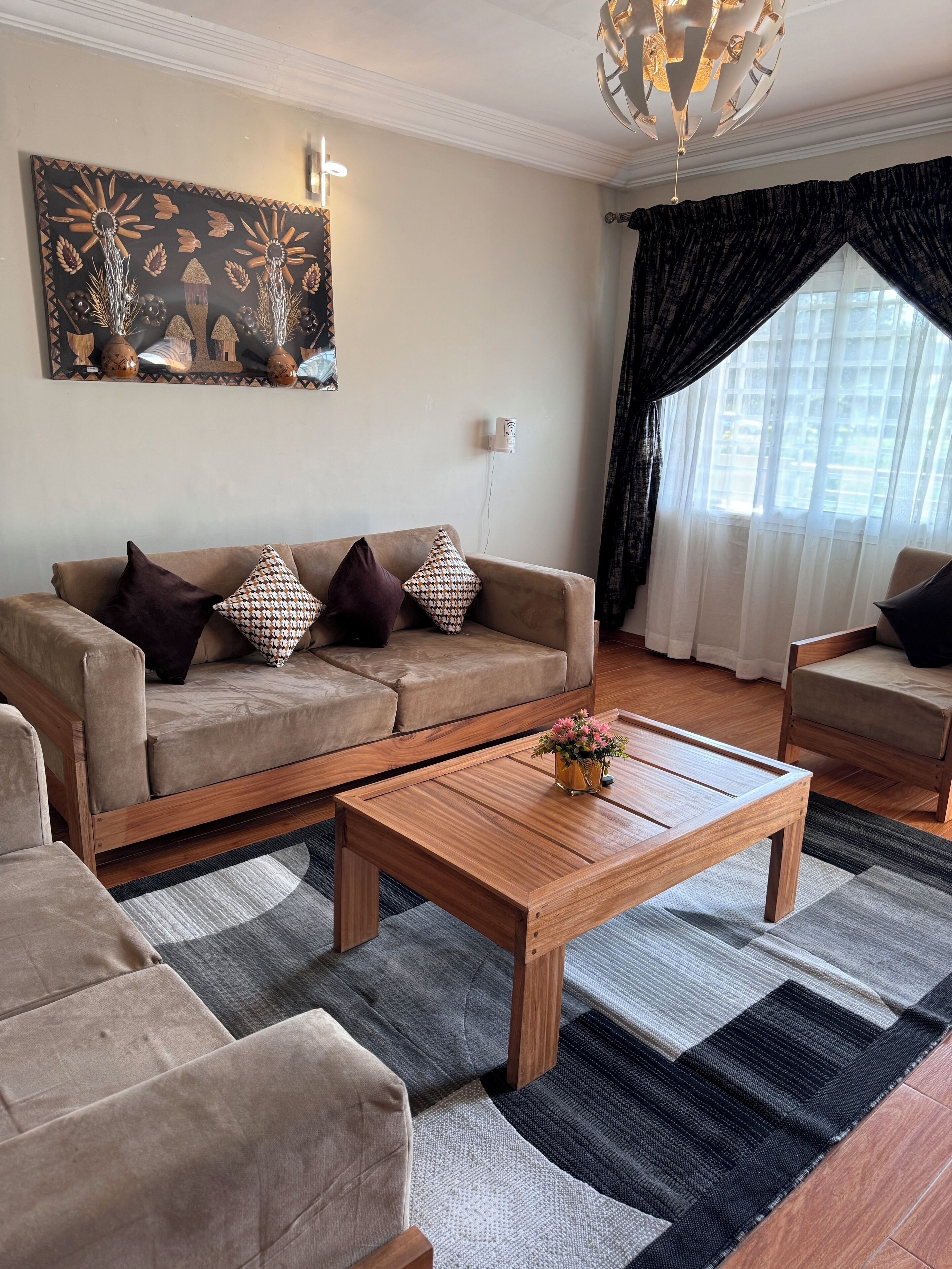 Una sala de estar con un sofá color beige, cojines estampados, una mesa de centro de madera y un cuadro abstracto grande en la pared.