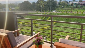 A balcony with wooden furniture and a flower pot, overlooking a green landscape with a mountain in the background. - Akhard Haus (Buea)