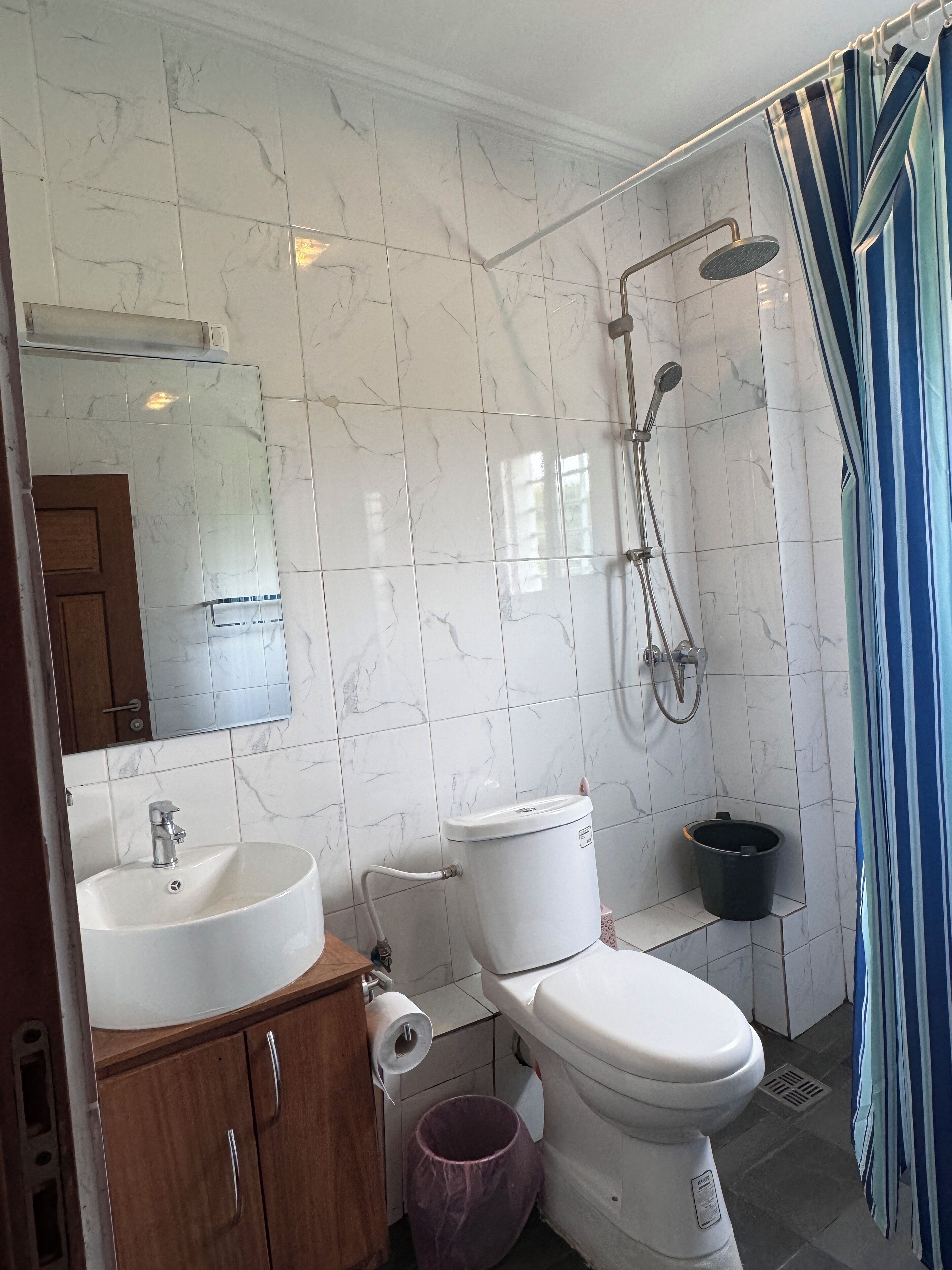 A bathroom with white marble tiles, a sink, a toilet, a shower, and a mirror.