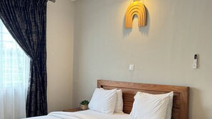 A neatly made bed with white linens, a wooden headboard, and a bedside table with a plant. - Akhard Haus (Buea)