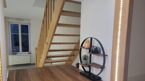 A modern interior with a wooden staircase, a wooden floor, and a wall-mounted shelf with decorative items. - Spacious duplex at Matthieu's. Sleeps 1 to 6. (Remiremont)