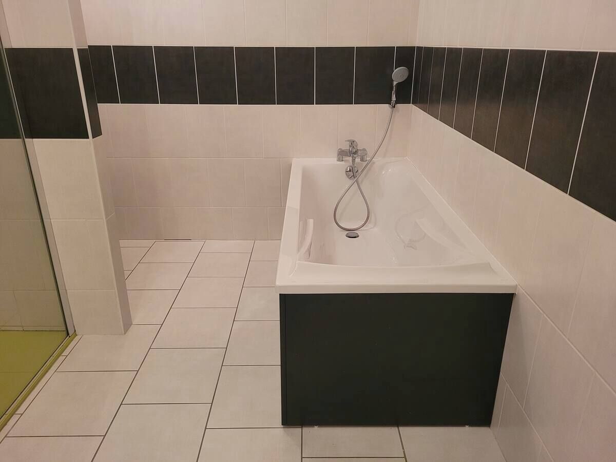 Een badkamer met een bad, wandtegels in het wit en zwart, en een betegelde vloer.