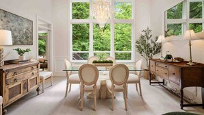 Un espace repas avec une table et des chaises en verre, entouré de grandes fenêtres offrant une vue sur la verdure.