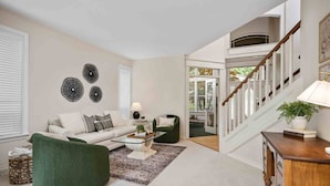 Un salon spacieux avec un fauteuil vert, un canapé blanc et une table basse. Un escalier mène à un niveau supérieur.
