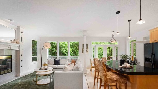 Une cuisine moderne dotée d’un îlot central, un coin repas avec des chaises en osier et un espace salon confortable avec un canapé et une table basse.