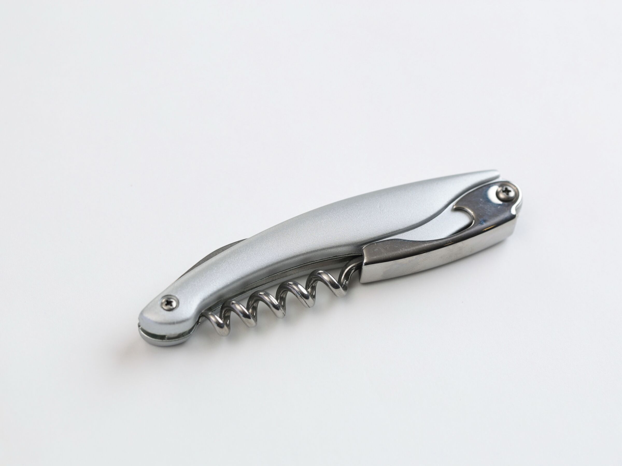 A metallic folding knife with a serrated edge and a screw mechanism.