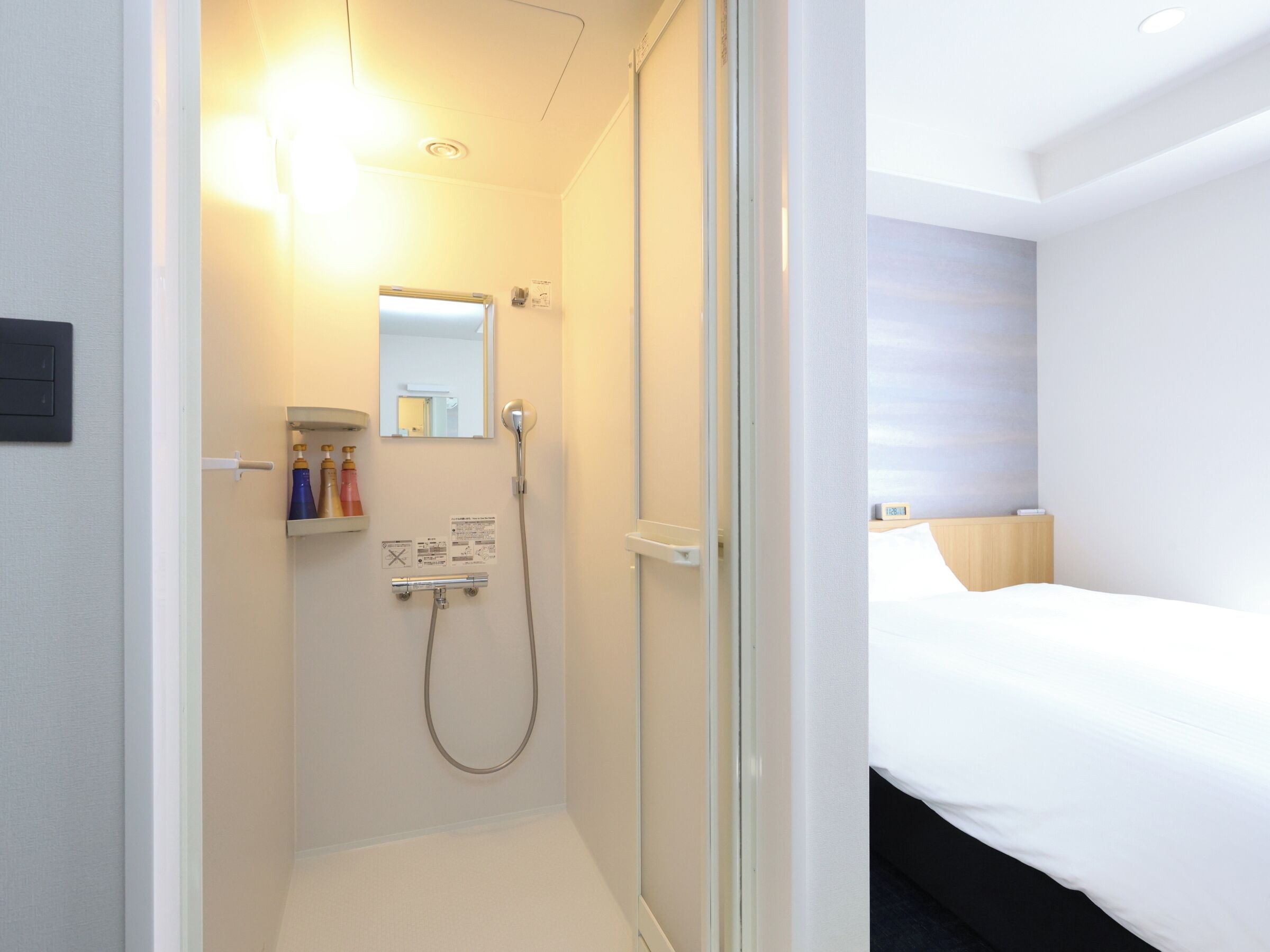 A hotel room with a shower, a bed, and a bedside table.