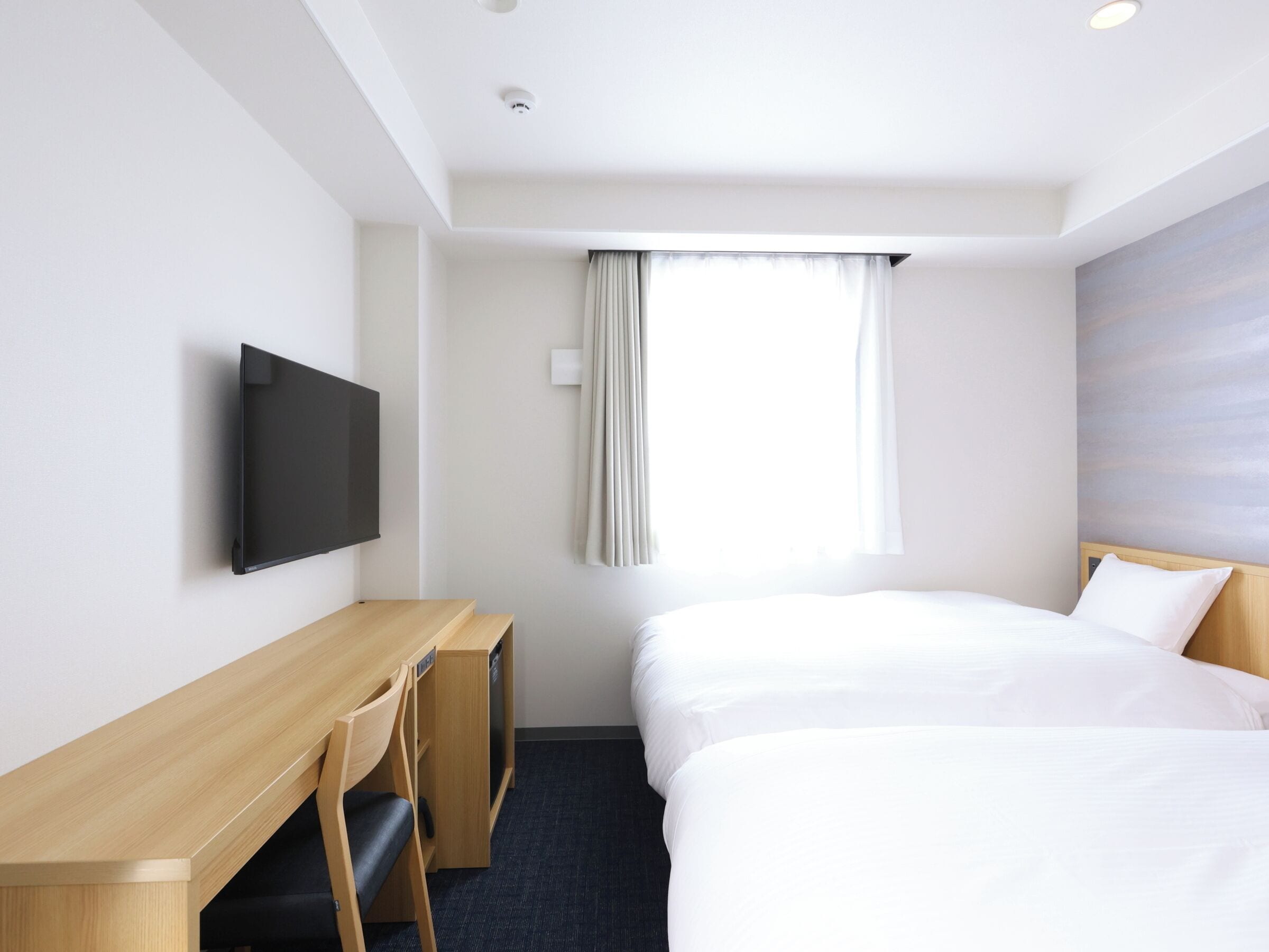 A hotel room with a bed, a desk, a chair, a television, and a window with curtains.
