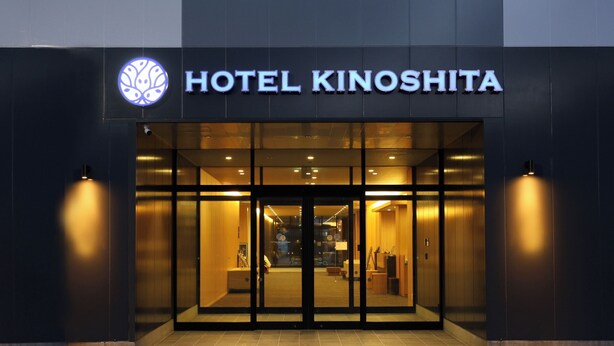 A entrada do Hotel Kinoshita, com fachada de vidro moderna e sinalização iluminada.