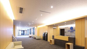 Uma área de recepção de hotel, com balcão, espaço para sentar e um quiosque de check-in.