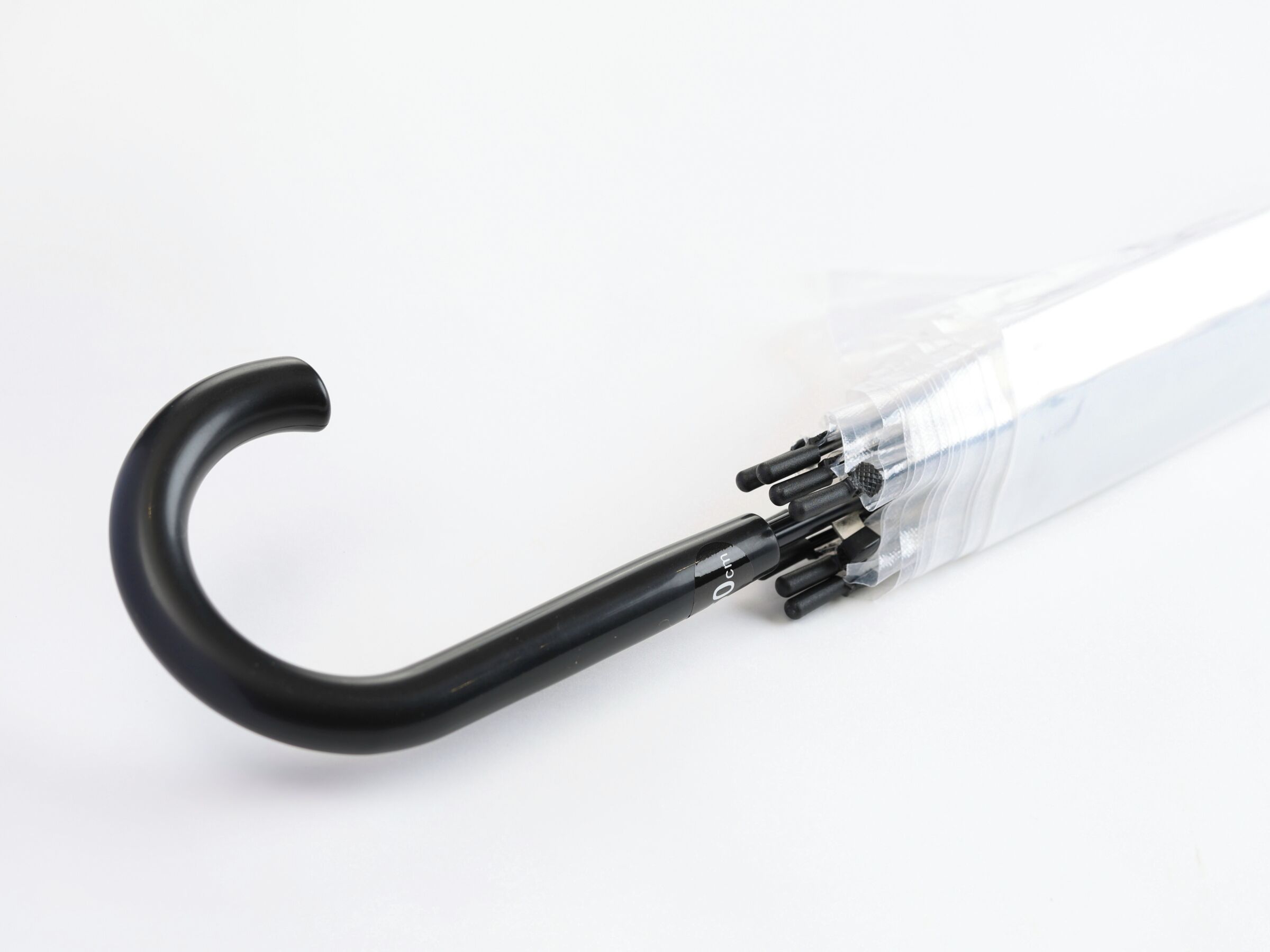 A clear plastic umbrella with a black handle and a visible metal spiral mechanism.