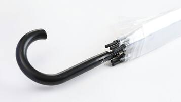 A clear plastic umbrella with a black handle and a visible metal spiral mechanism.