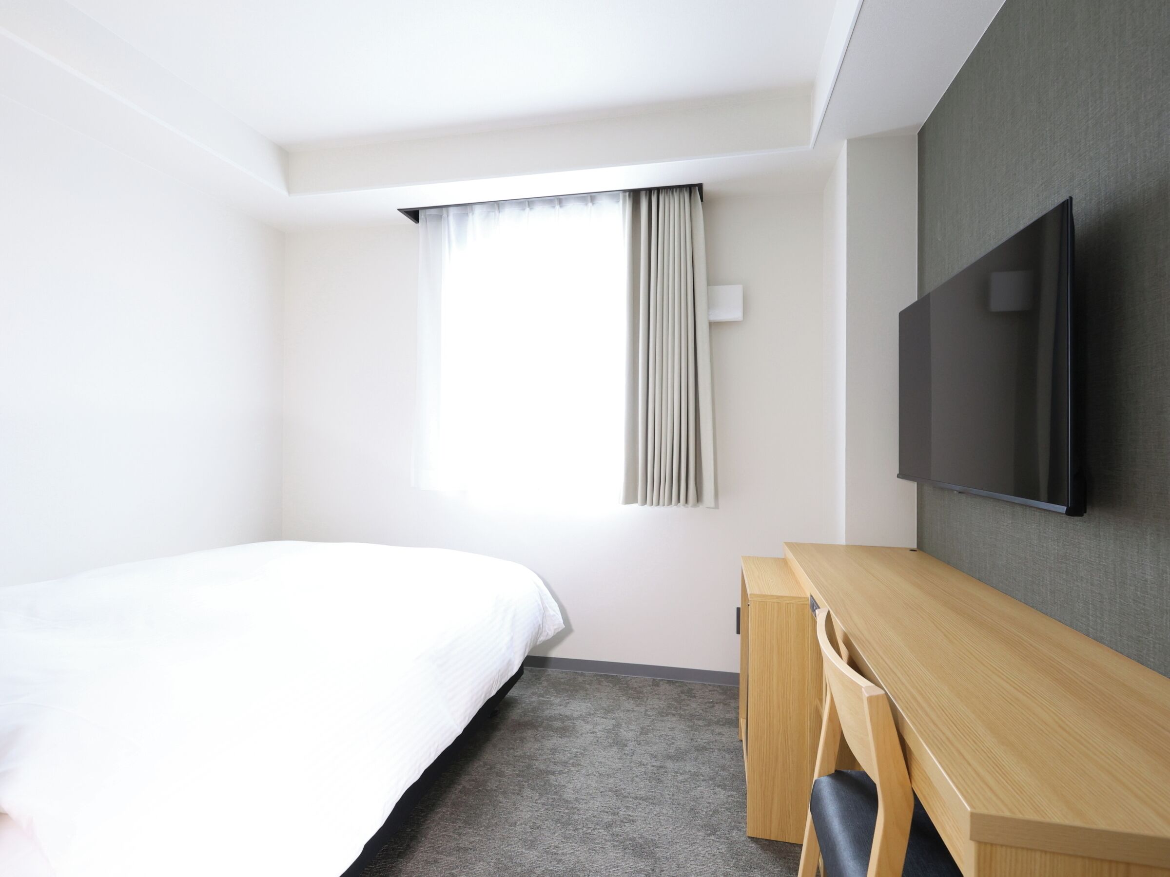 Habitación de hotel con cama, escritorio, silla, televisor y ventana con cortinas.