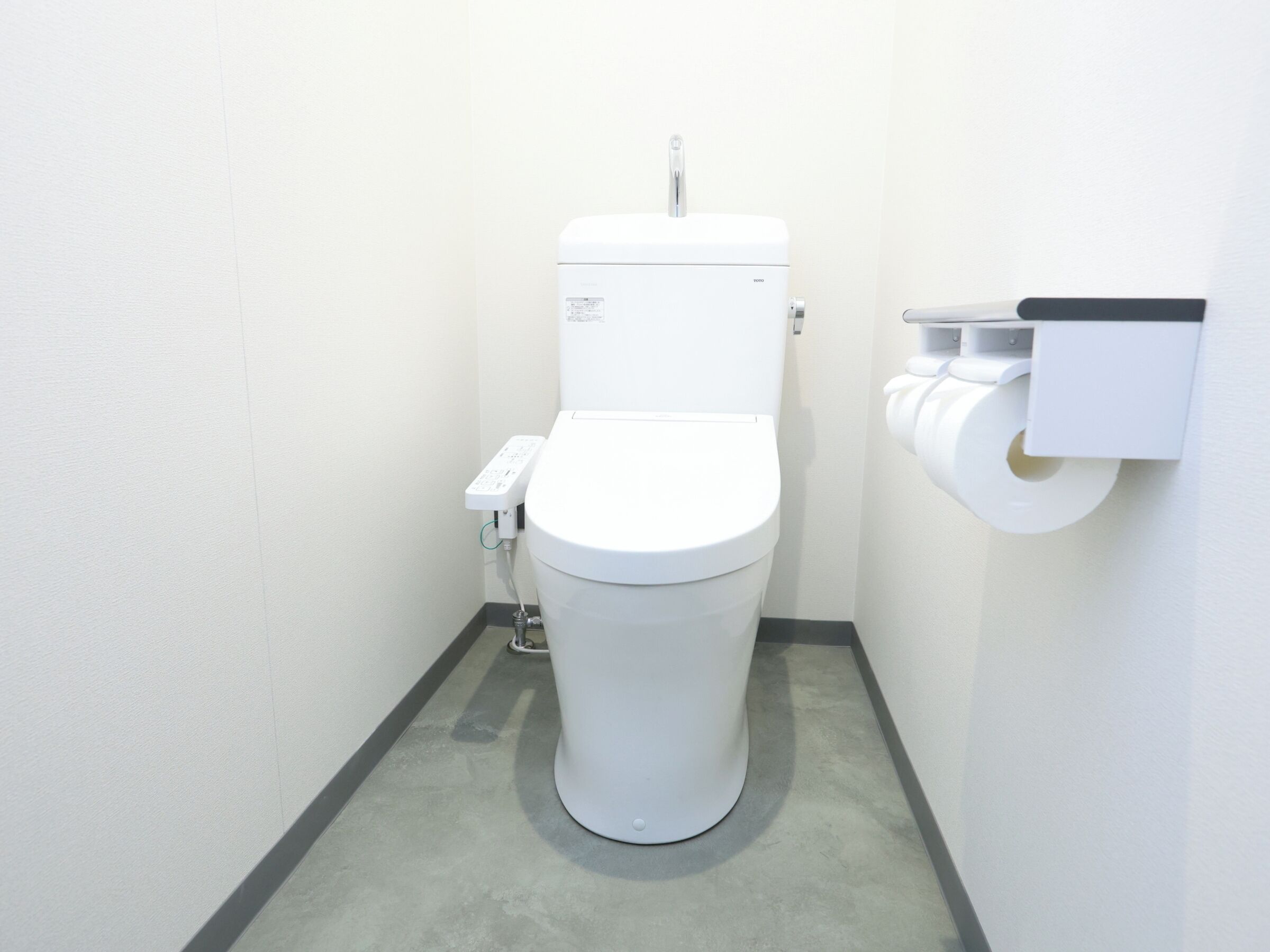 A white toilet with a flush handle and a paper towel dispenser mounted on the wall.