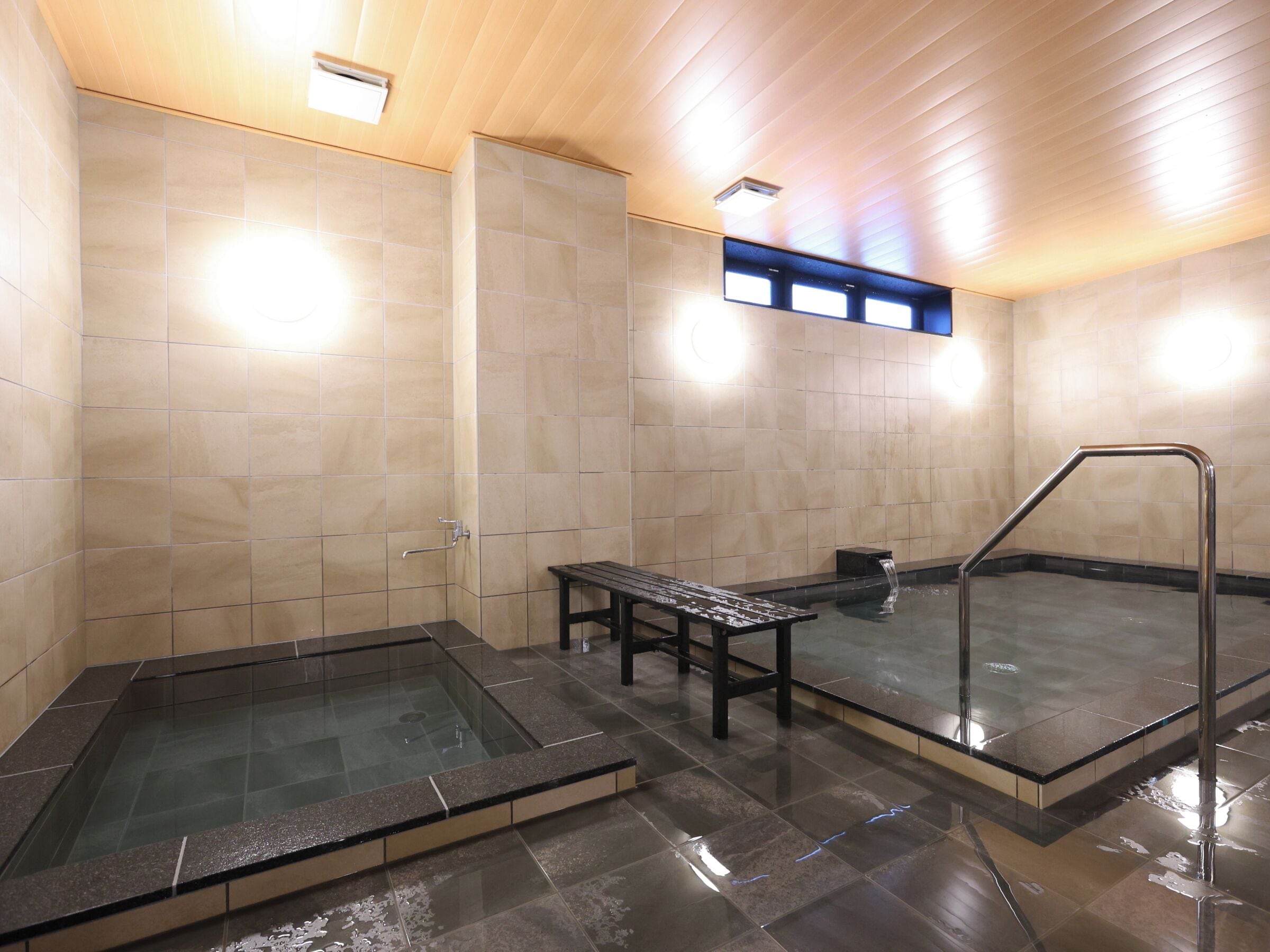 A modern indoor pool area with a glass-enclosed hot tub, a seating bench, and a separate hot tub area.