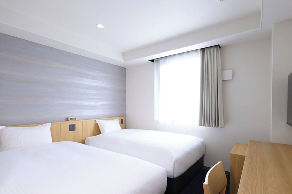 A hotel room with two beds, a desk, and a large window with curtains.