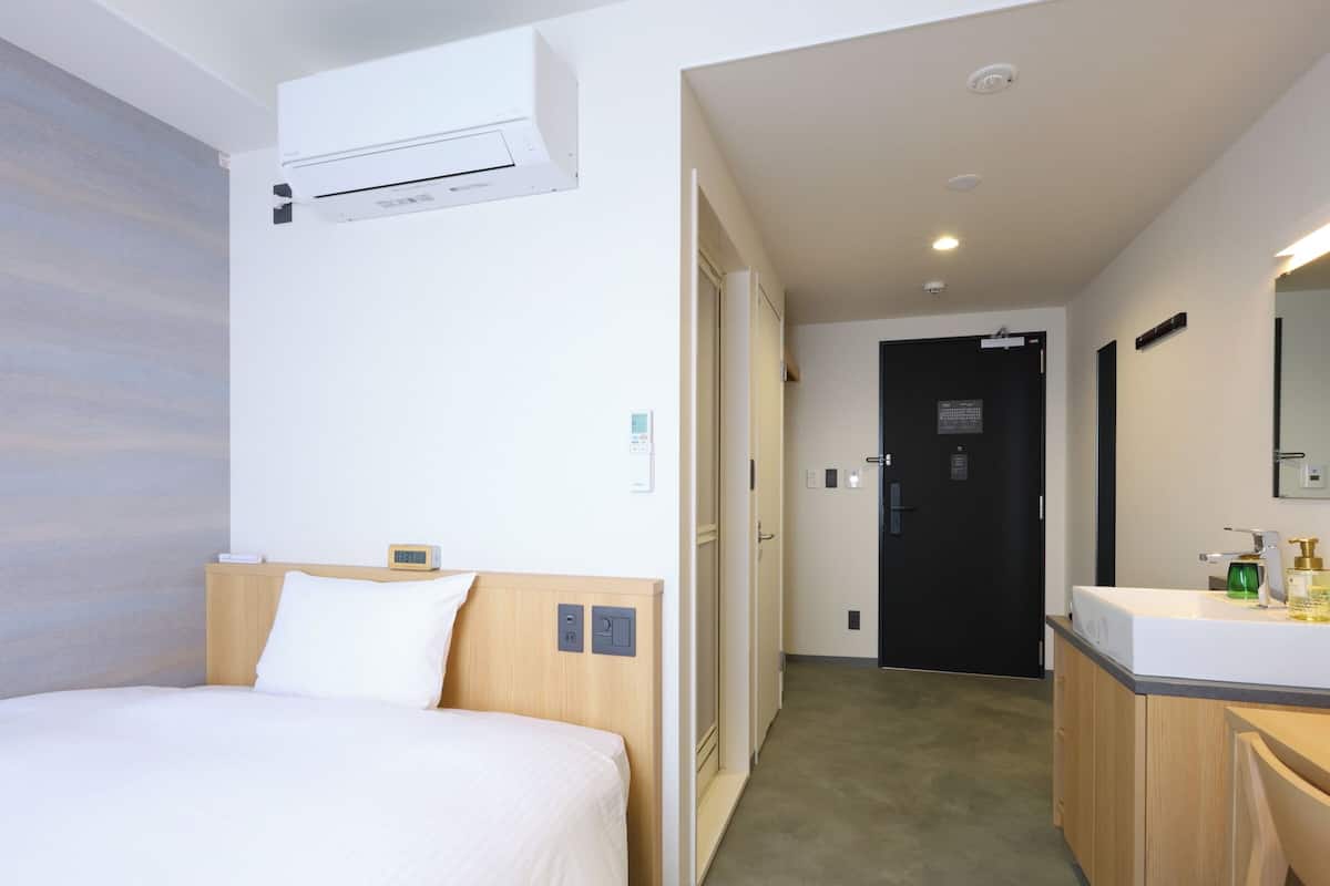 A hotel room with a bed, bedside table, and a bathroom with a sink and mirror.