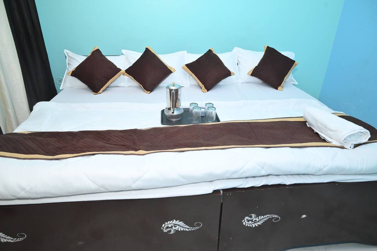 Ein ordentlich bezogenes Bett mit weißer und brauner Bettwäsche, ein Tablett mit Kaffeekanne und Gläsern sowie ein dunkles Holz-Kopfteil mit dekorativen Schnitzereien.