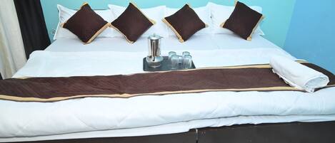 A neatly made bed with white and brown bedding, a tray with a coffee pot and glasses, and a dark wooden headboard with decorative carvings.