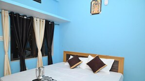 A neatly made bed with a tray of glasses and a pitcher, a window with black and beige curtains, and a framed picture on the wall. - Shri Sita Vallabh Padchhaya (Ayodhya)
