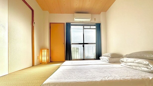 A room with tatami mats, a bed with white bedding, a sliding door, and a ceiling-mounted air conditioner. - [ 303 ] Twin Japanese-style room with kitchen, bathroom and washing machine, 2 min. from the nearest station, along the airport line. (大阪市)