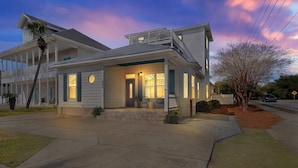 A two-story house with a balcony, a porch with seating, and a well-lit entrance.