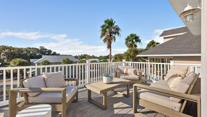 A wooden deck with outdoor furniture, including sofas and a table, overlooking a residential area with houses and palm trees.