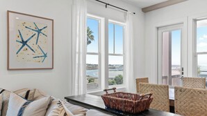 Ein modernes Wohnzimmer mit großem Fenster, einem gerahmten abstrakten Gemälde und einem Korbstuhl-Beistelltisch.