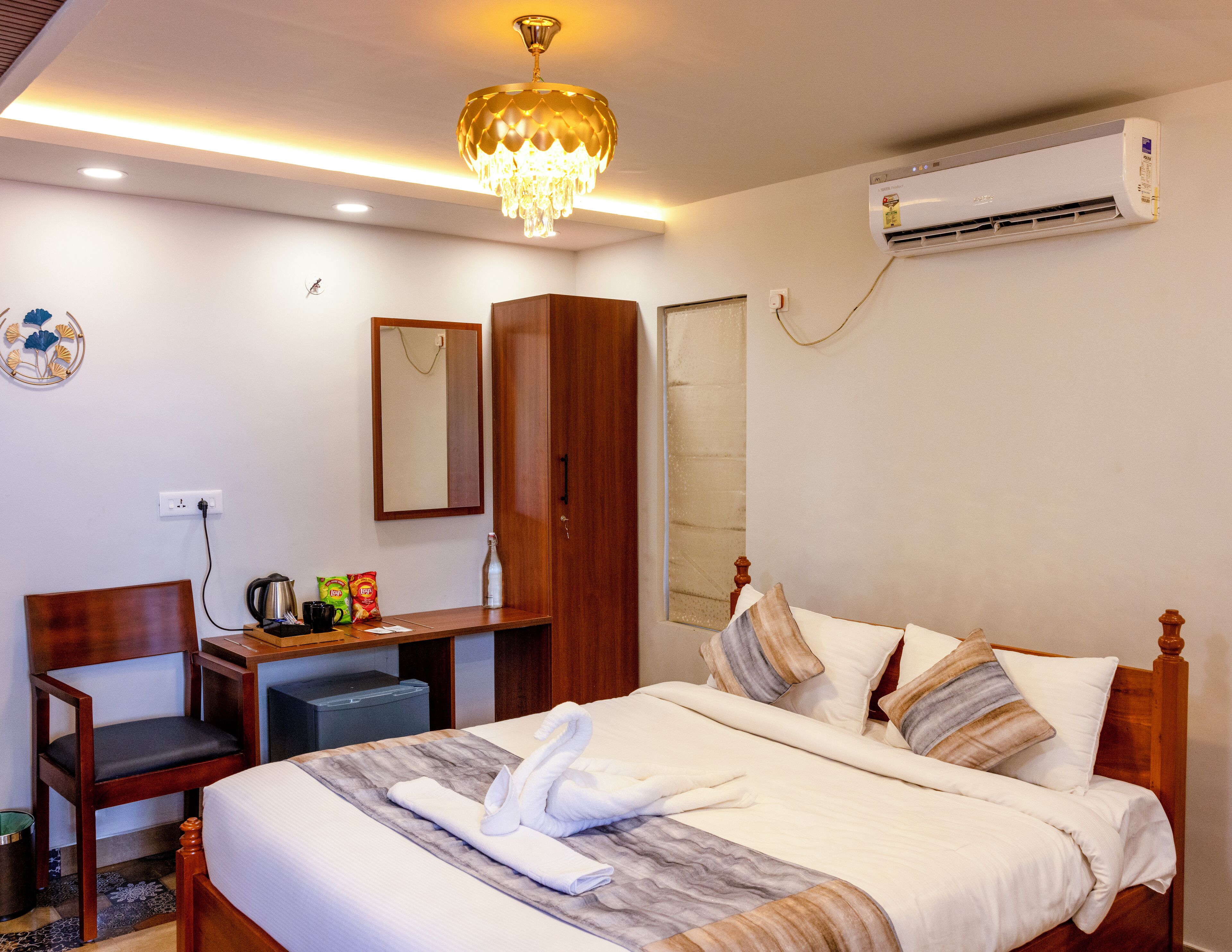 Habitación de hotel con cama, armario de madera, escritorio con silla, espejo, equipo de aire acondicionado y candelabro.