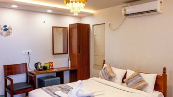 Habitación de hotel con cama, armario de madera, escritorio con silla, espejo, equipo de aire acondicionado y candelabro.